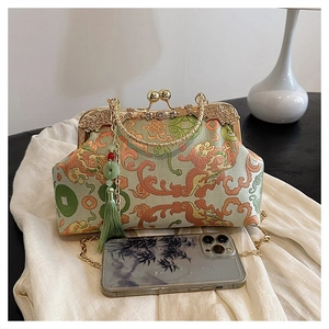 Detailed view of green silk embroidery bag with tassel and chain next to a phone