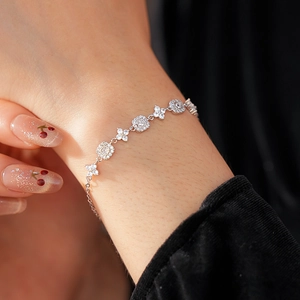 Detail of silver clover and square zircon bracelet on wrist with elegant lighting