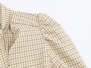 Detail view of beige plaid blouse featuring pleated puff shoulder and refined neckline