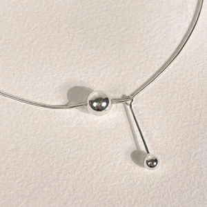 Macro detail of silver snake chain necklace with metallic beads and cylinder pendant