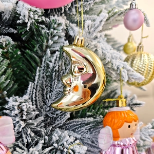 Gros plan d'une décoration de Noël lune dorée parmi des boules roses et des branches
