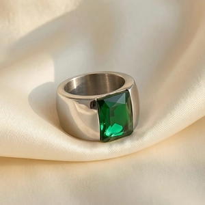 Close-up of titanium steel ring with rectangular emerald-cut green stone on beige silk