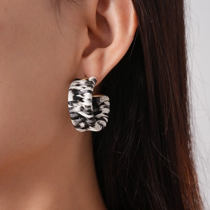 Detail shot of a black and white woven C-shaped earring worn by a model in soft lighting