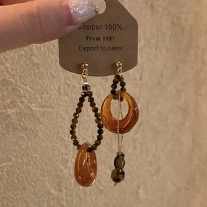 Détail de boucles d'oreilles asymétriques en résine et cuivre avec effet ambre