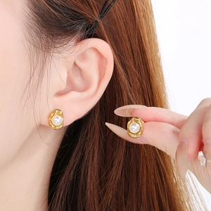 Detailed close-up of golden irregular round stud earrings with white pearls on a model
