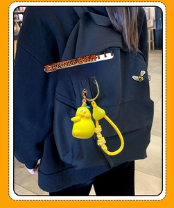 Detail of yellow cartoon pear keychain hanging on a black backpack with gold hardware