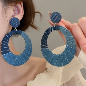 Detailed view of large oval denim fabric drop earrings with multi-tone blue patchwork textures