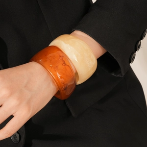 Detail of chunky resin bangles in amber and ivory tones worn over a black blazer