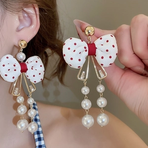 Detailed view of red polka dot bow earrings with hanging pearls and zircon accents