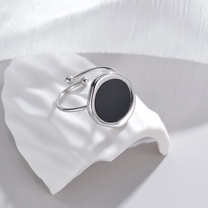 Detail view of silver open ring with black circular inlay on minimalist white background