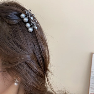 Detail of mini metallic bow hair claws with white pearls worn on a model's side hair