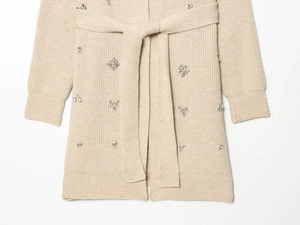 Détail du cardigan beige en maille avec flocons en strass brillants et ceinture à la taille