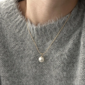 Elegant minimalist white pearl pendant necklace with gold chain worn on gray sweater