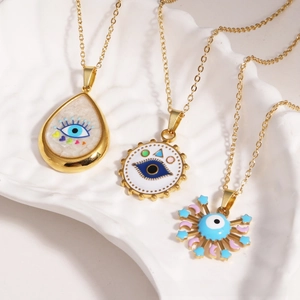 Macro detail of gold-plated evil eye pendants on a white ceramic tray with fine O-chains