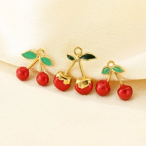 Detailed view of red cherry charms with gold stems on a beige silk background