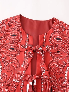 Detail of red paisley print vest featuring a front tie bow and round neckline design