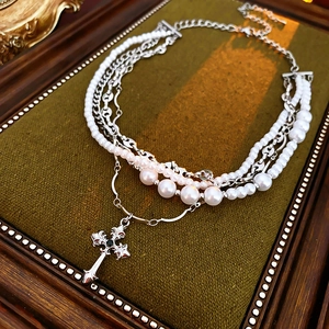 Detail of layered pearl necklace with silver cross pendant on green velvet background