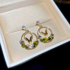 Detailed shot of gold butterfly hoop earrings with green zircon floral accents in jewelry box