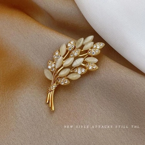 Detailed close-up of golden wheat brooch with sparkling cat eye stones on silk fabric
