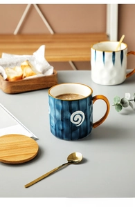Detail of Japanese ceramic mug with blue spiral pattern, wooden lid, and gold spoon