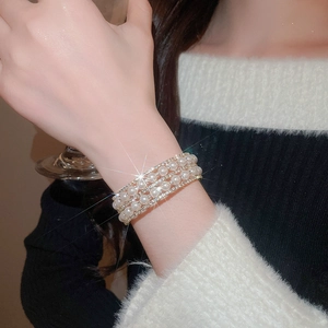 Close-up of layered pearl and rhinestone bracelet on wrist in elegant gold finish
