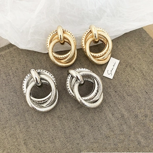 Detailed close-up of textured triple-layer interlocking metal earrings in gold and silver