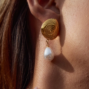 Detail of gold spiral metal earring with teardrop pearl on female model