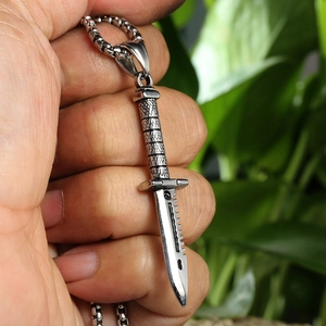 Close-up of a silver stainless steel dagger pendant necklace held in a hand