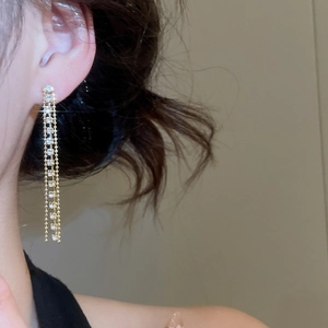 Dettaglio di orecchini a frangia dorati con cristalli scintillanti su modella