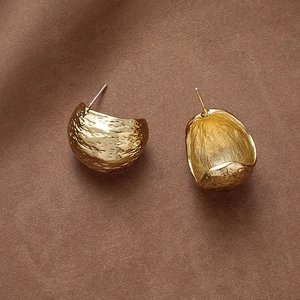 Macro detail of golden C-shape geometric earrings with textured hammered finish on satin