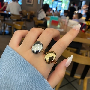 Minimalist gold and silver polished pebble rings set on model's hand in casual setting