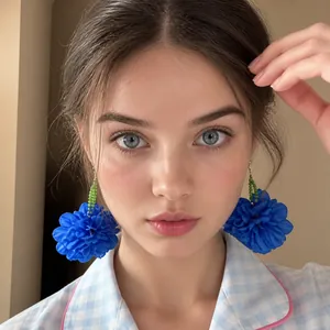 Close-up of oversized blue fabric flower earrings with red bead accents on a model
