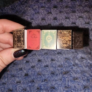 Macro shot of five vintage miniature books held by hand, showing fine printed details