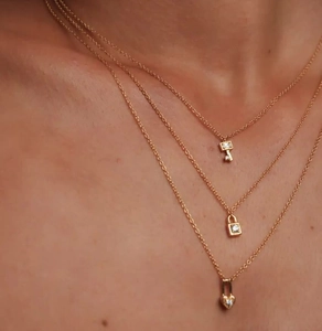 Close-up of layered gold necklace set with sparkling heart, lock and key charms