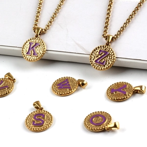 Detail of round gold stainless steel pendants with purple enamel letters on marble