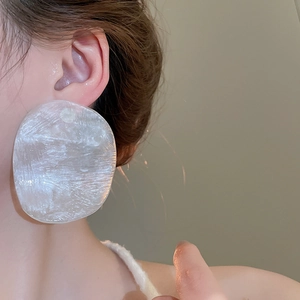 Close-up of oversized white resin oval earrings with brushed texture on female model