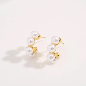 Elegant gold C-shaped hoop earrings with white pearls on a clean white reflective background