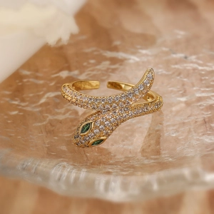 Detailed view of a gold snake ring with green gem eyes and crystals on a glass tray