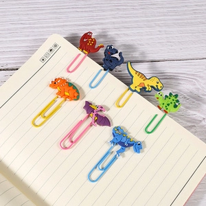 Close-up of 6 colorful dinosaur paper clips with soft rubber icons on a notebook page