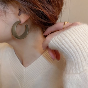 Detail view of a glossy dark olive green C-shaped hoop earring on female model