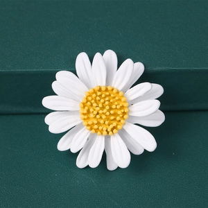 Macro shot of white enamel daisy brooch with yellow center on dark green background