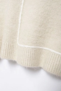 Detail view of cream knit sweater showing soft fabric texture and white line stitching