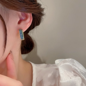 Detail of elegant gold geometric hoop earrings with inlaid blue and green zircon stones