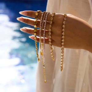 Detail of five gold-plated heart zircon bracelets worn on hand by a blue swimming pool