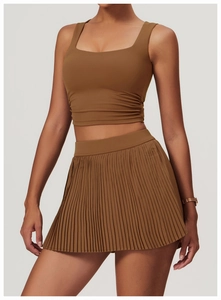 Detail of caramel brown tennis skirt set featuring side ruched top and pleated hemline