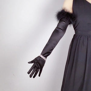 Detail of long black satin gloves featuring elegant feather trim and a smooth finish