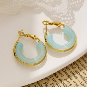 Detail of 18k gold plated hoop earrings with light blue resin drops on a white tray