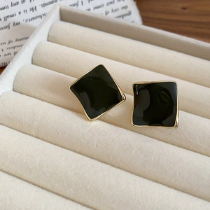 Macro shot of gold-plated square enamel earrings on a soft beige velvet jewelry box