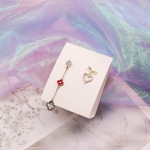 Gold asymmetrical earrings with red clover and heart diamond stud on white card