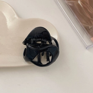 Minimalist black acrylic hair claw clip with geometric hollow design on a cream tray